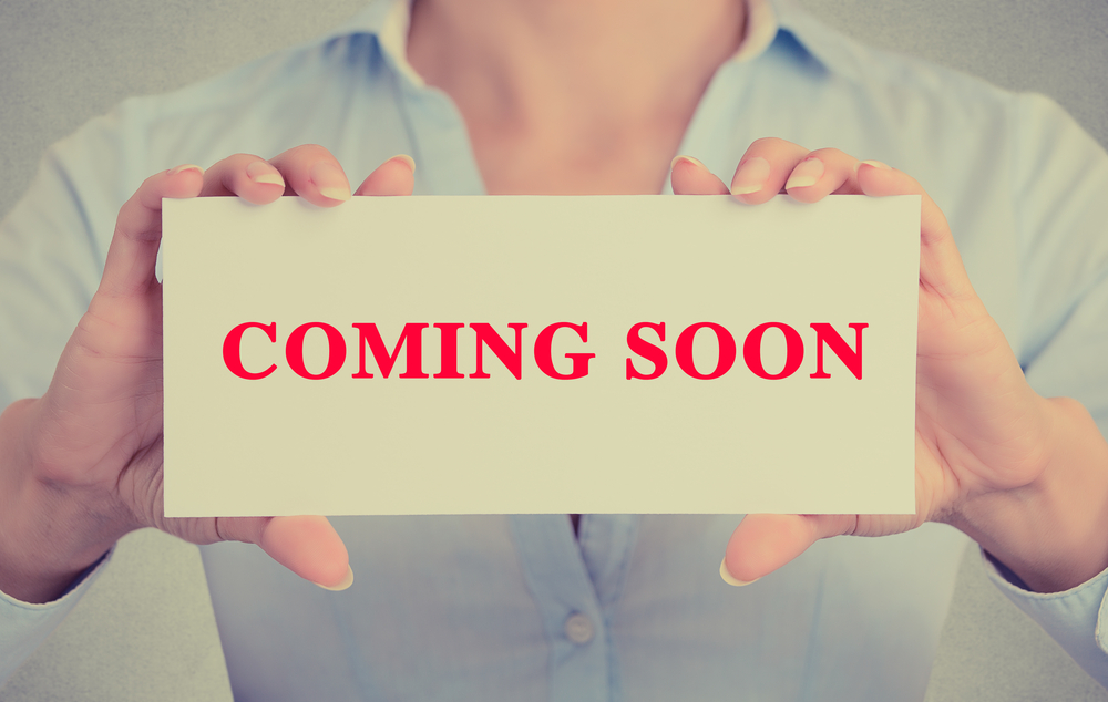 Businesswoman hands holding white card sign with coming soon text message isolated on grey wall office background. Retro instagram style image Businesswoman hands holding white card sign with coming soon text message isolated on grey wall office background. Retro instagram style image